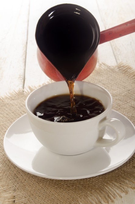 coffee is filled from a red small metal pot in a cup