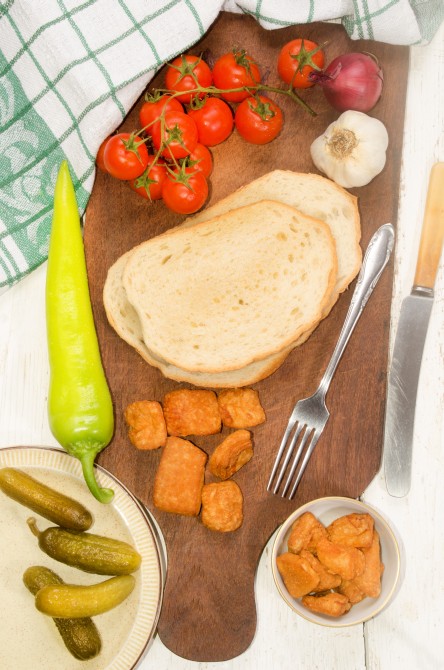 hungarian breakfast with home made bread, crackling, cherry tomato, onion, garlic, gherkin, fork and knife on wooden board 