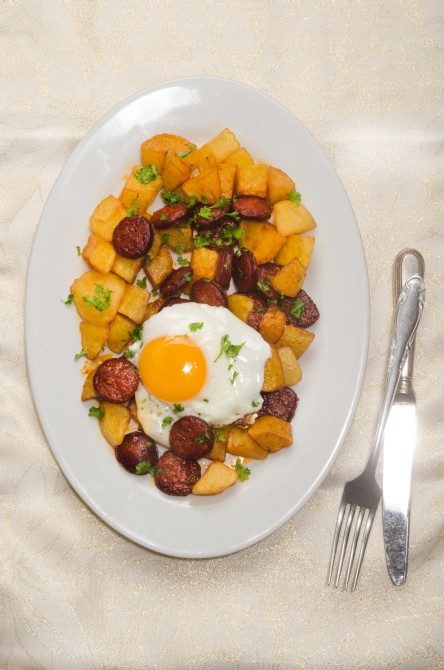 spanish meal with sliced chorizo, roasted potato, fried egg and parsley on a plate