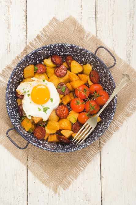 spanish country style meal with potato, cherry tomato, fried egg, parsley and chorizo in a pan