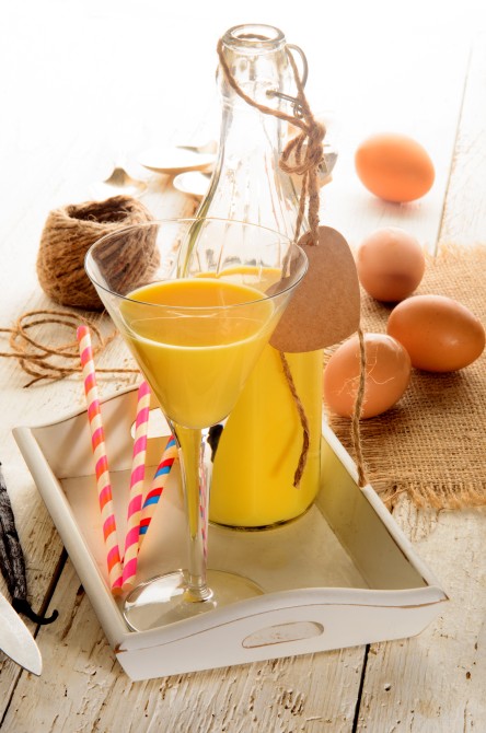 egg liqueur in a cocktail glass and a glass bottle, eggs, vanilla beans, straw on serving tray