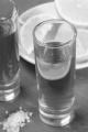 tequila in a shot glass, coarse salt on slate and lemon slice on a plate in the background